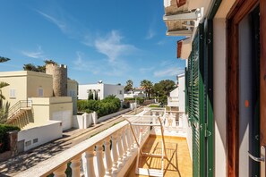 A residential area with white buildings, a stone tower, and a balcony with a wooden floor. - Apartamentos Mar Blanca (Ciutadella de Menorca)