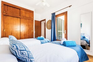 A hotel room with two beds, wooden wardrobes, a ceiling fan, and a window with blinds. - Apartamentos Mar Blanca (Ciutadella de Menorca)