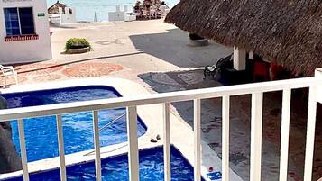 A pool area with a view of the sea, a thatched-roof structure, and a building with a balcony.