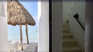 Vista a la playa con un paraguas de paja y una escalera que da al interior.