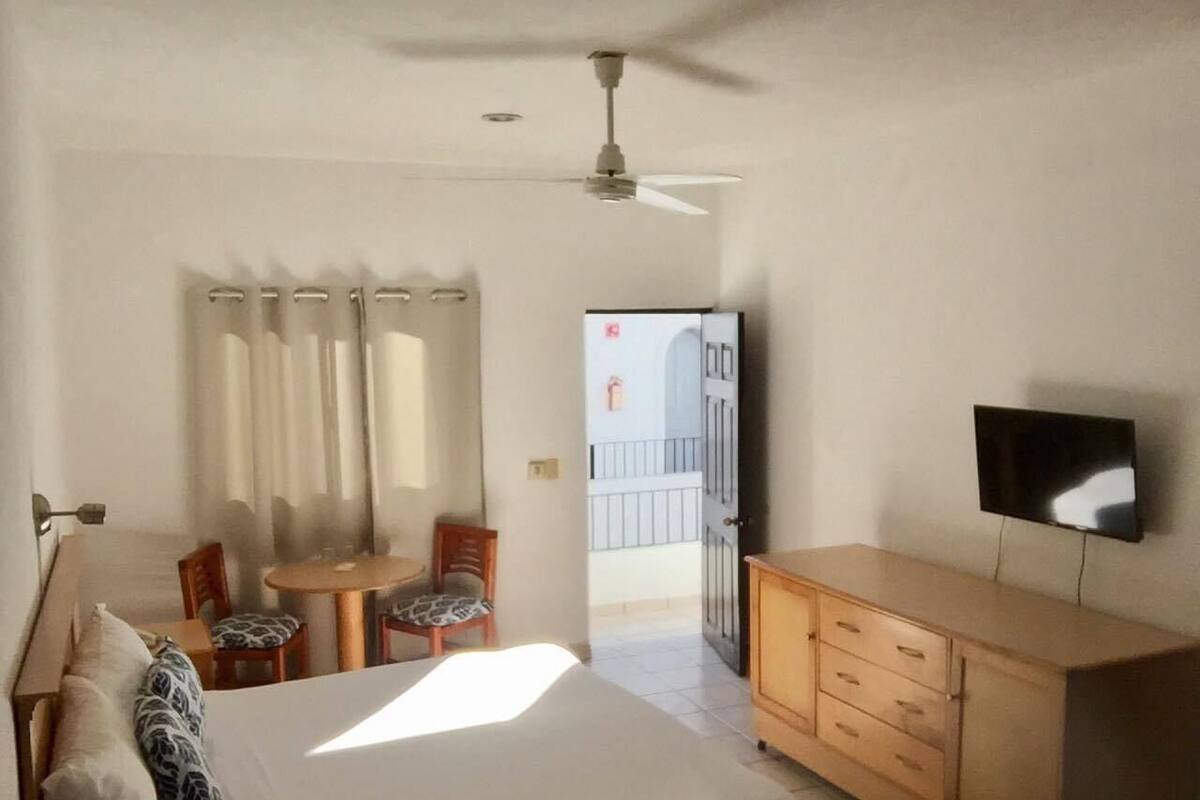 A hotel room with a bed, a desk with a chair, a television, and a wardrobe.