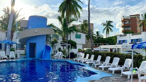 Una piscina con tobogán, rodeada de sillas de descanso y palmeras.