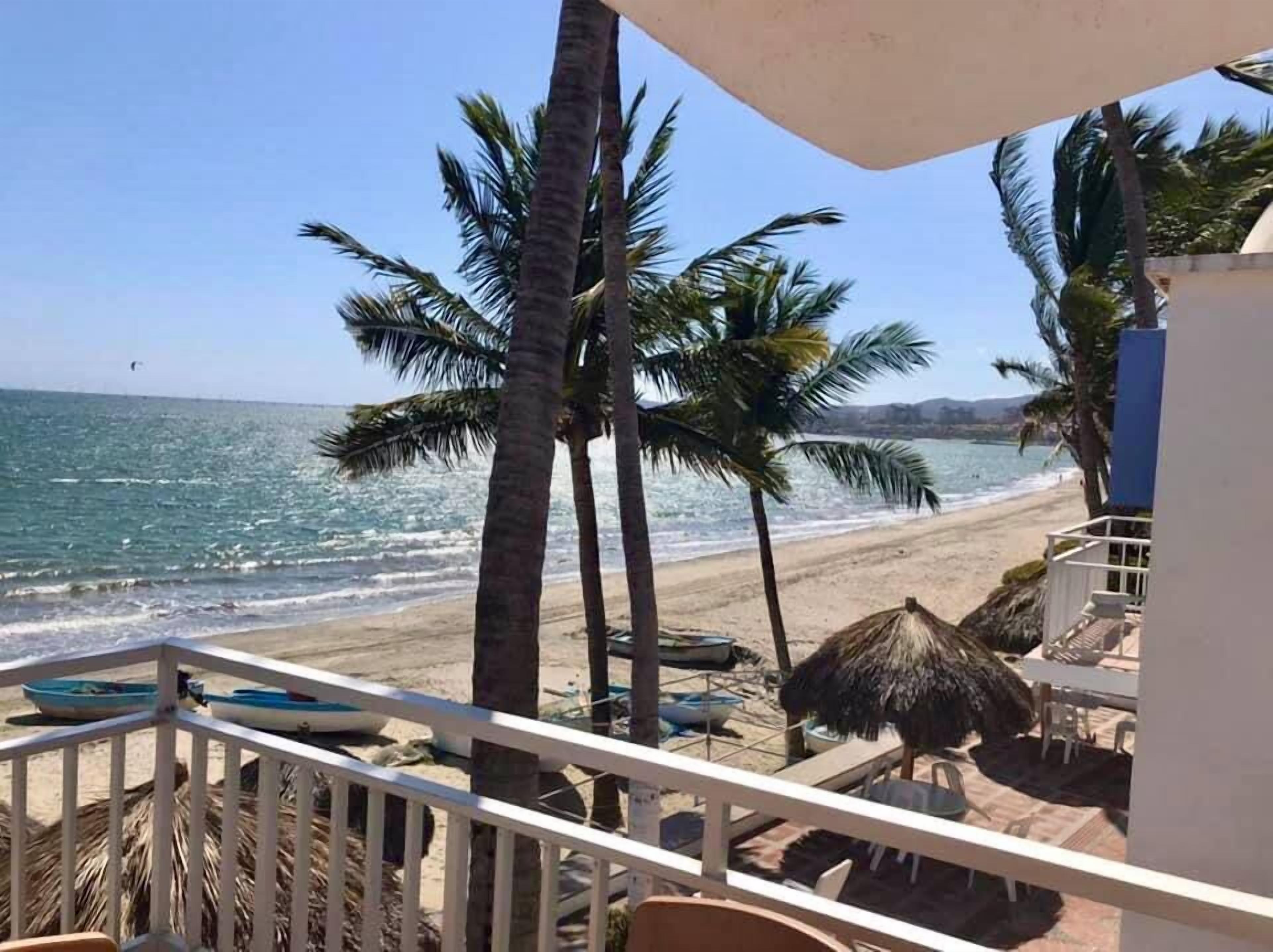 A balcony with a view of the beach, palm trees, and boats.