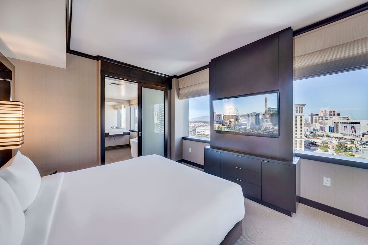 A modern hotel room with a large bed, a TV, and a city view.