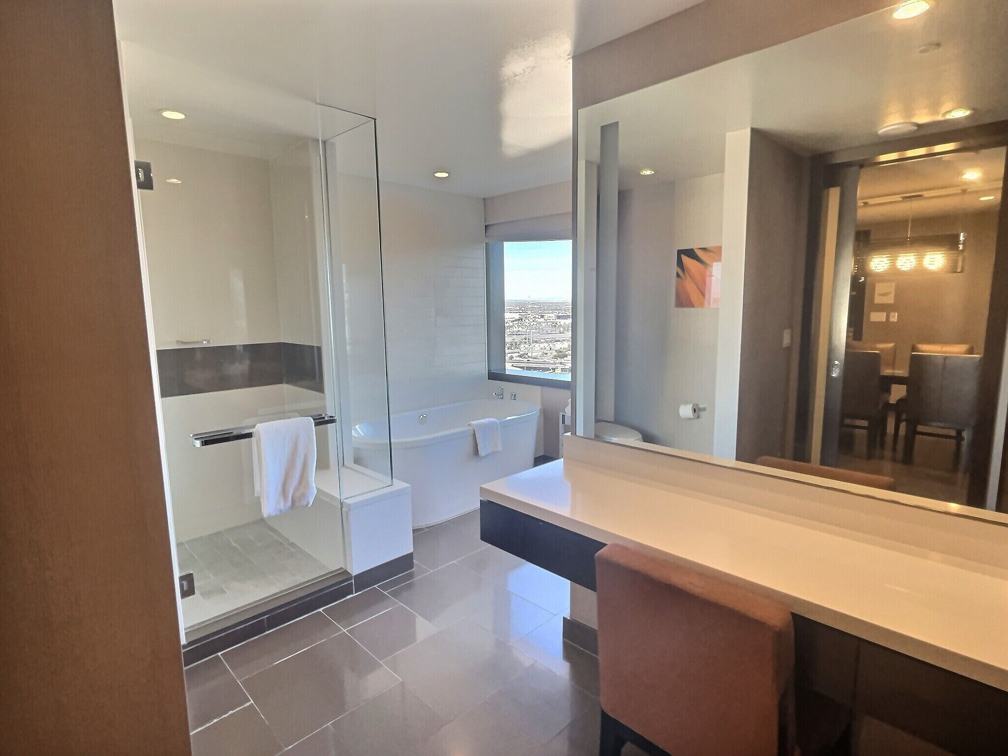 A modern bathroom with a glass-enclosed shower, a large mirror, and a view of the city through a window.