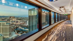 A hotel corridor with large windows offering views of a cityscape, including a prominent tower and a river.
