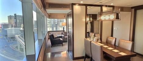 A modern hotel room with a dining area, large windows with a city view, and a balcony.