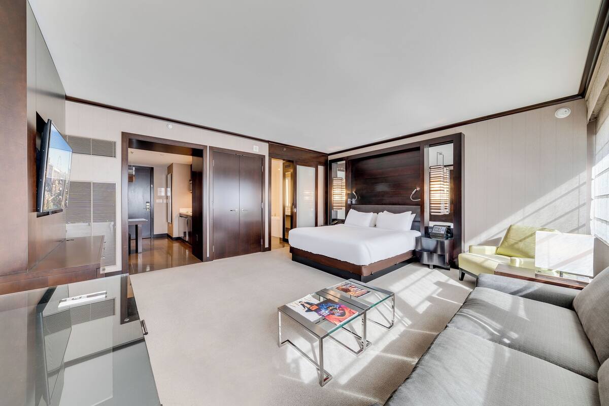 A modern hotel room with a large bed, a sofa, a glass coffee table, and a TV.