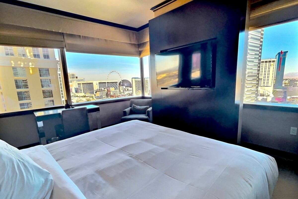 A hotel room with a large bed, a seating area, and a TV. The room has a city view.