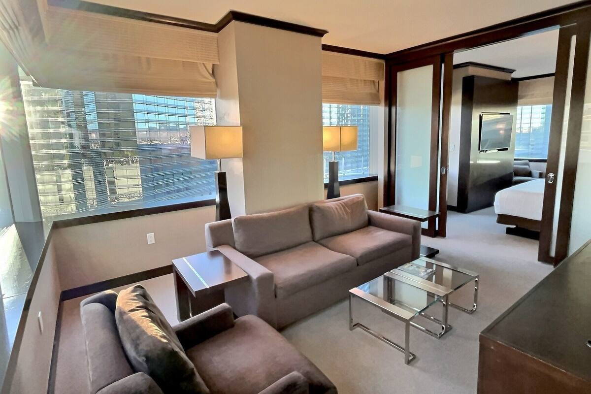 A modern hotel room with a sofa, a glass coffee table, and a bed.