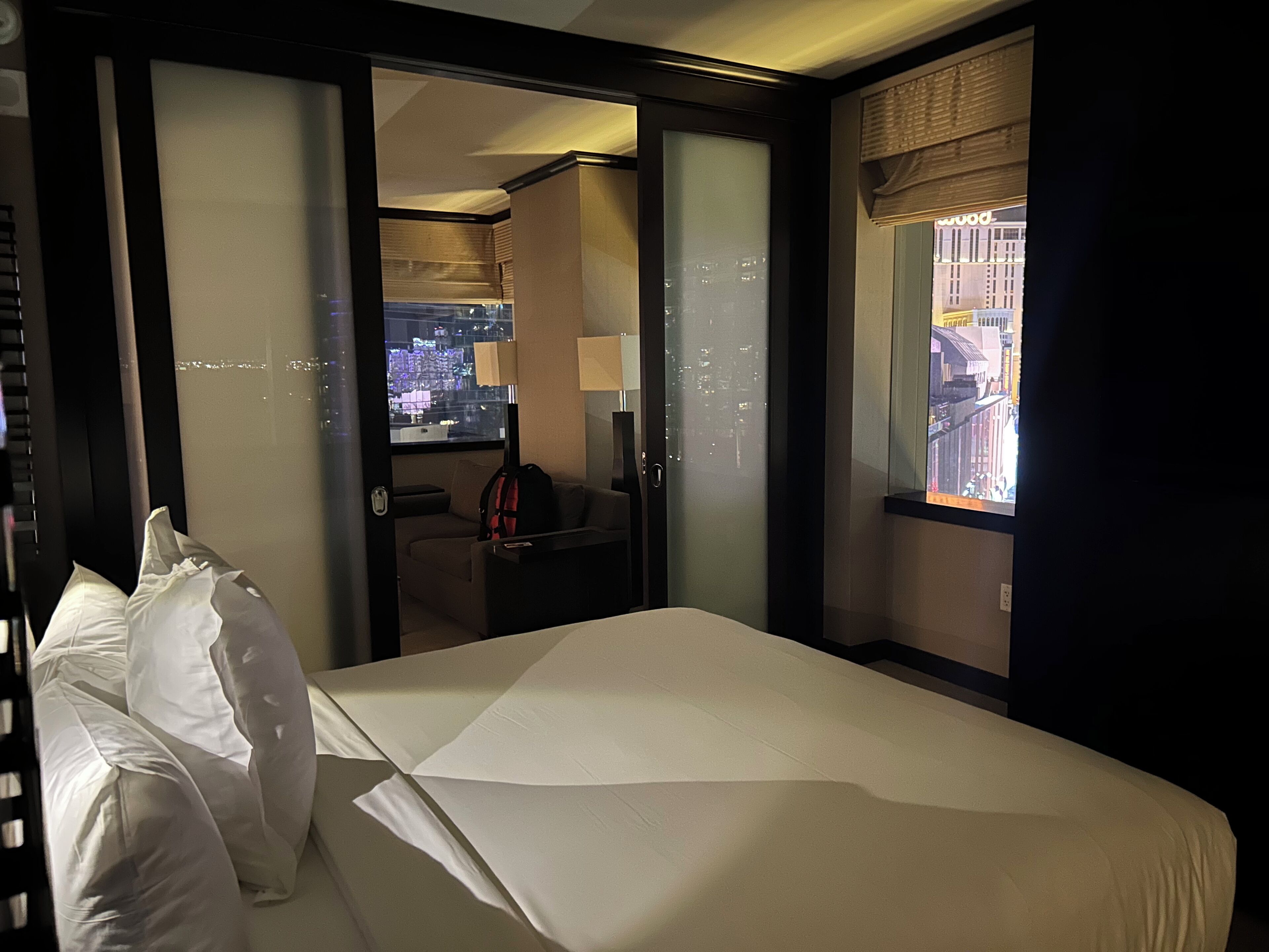 A hotel room with a bed, a desk, a chair, and a view of the city through the window.