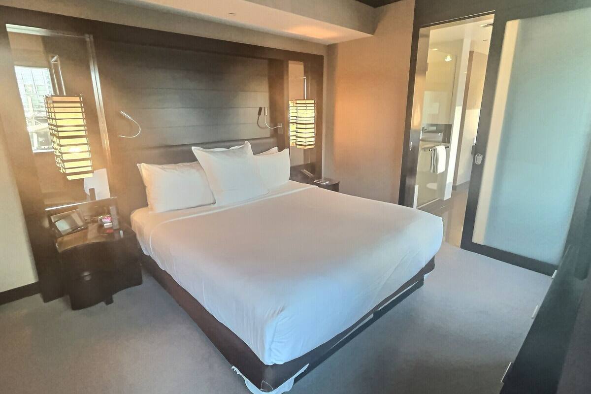 A hotel room with a large bed, bedside tables, a mirror, and a door leading to a bathroom.