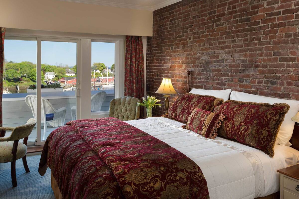 Habitación de hotel con una cama grande, una silla, una lámpara y vistas al exterior.