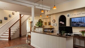 A reception area with a wooden staircase, a reception desk, and a wall-mounted television. - Lord Camden Inn (Camden)