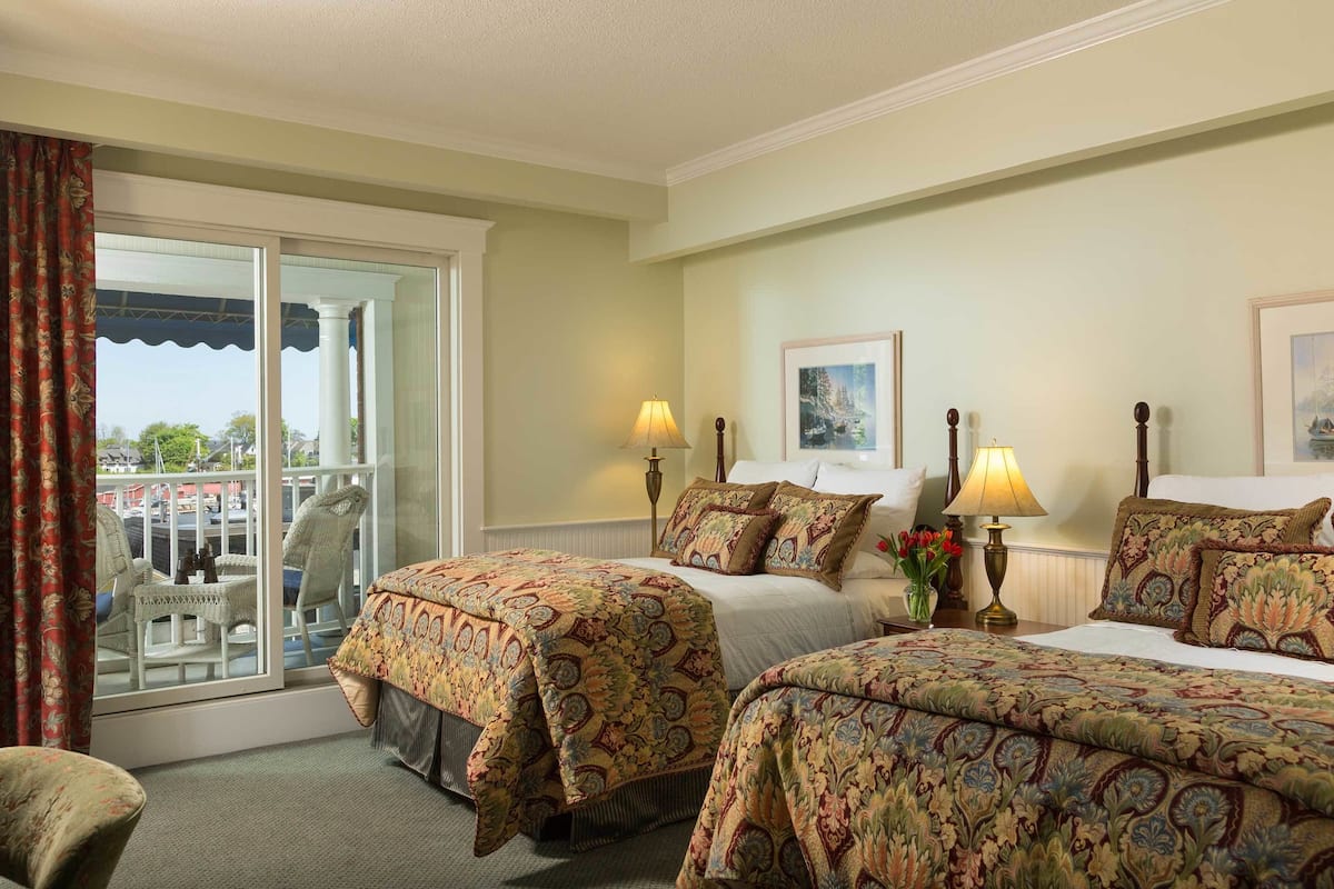 Habitación de hotel con dos camas, un balcón con vistas y una silla.
