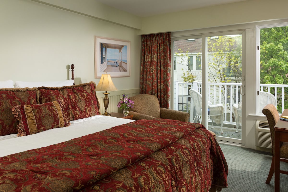 Habitación de hotel con una cama grande, una silla, una mesa y vistas al exterior a través de un ventanal corredero.