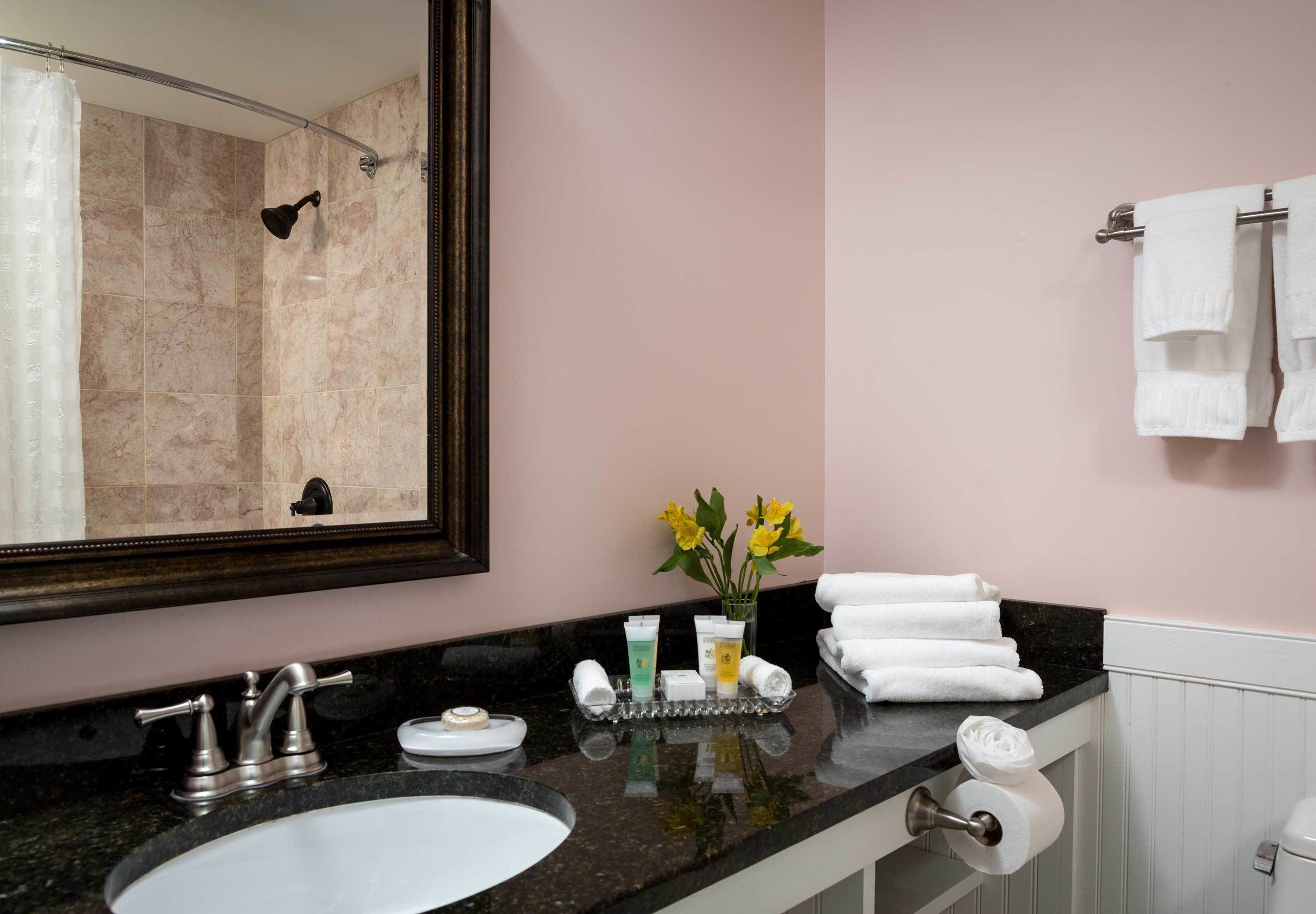 A bathroom with a marble shower, a large mirror, a sink with a faucet, a vanity with toiletries, and towels on a rack.