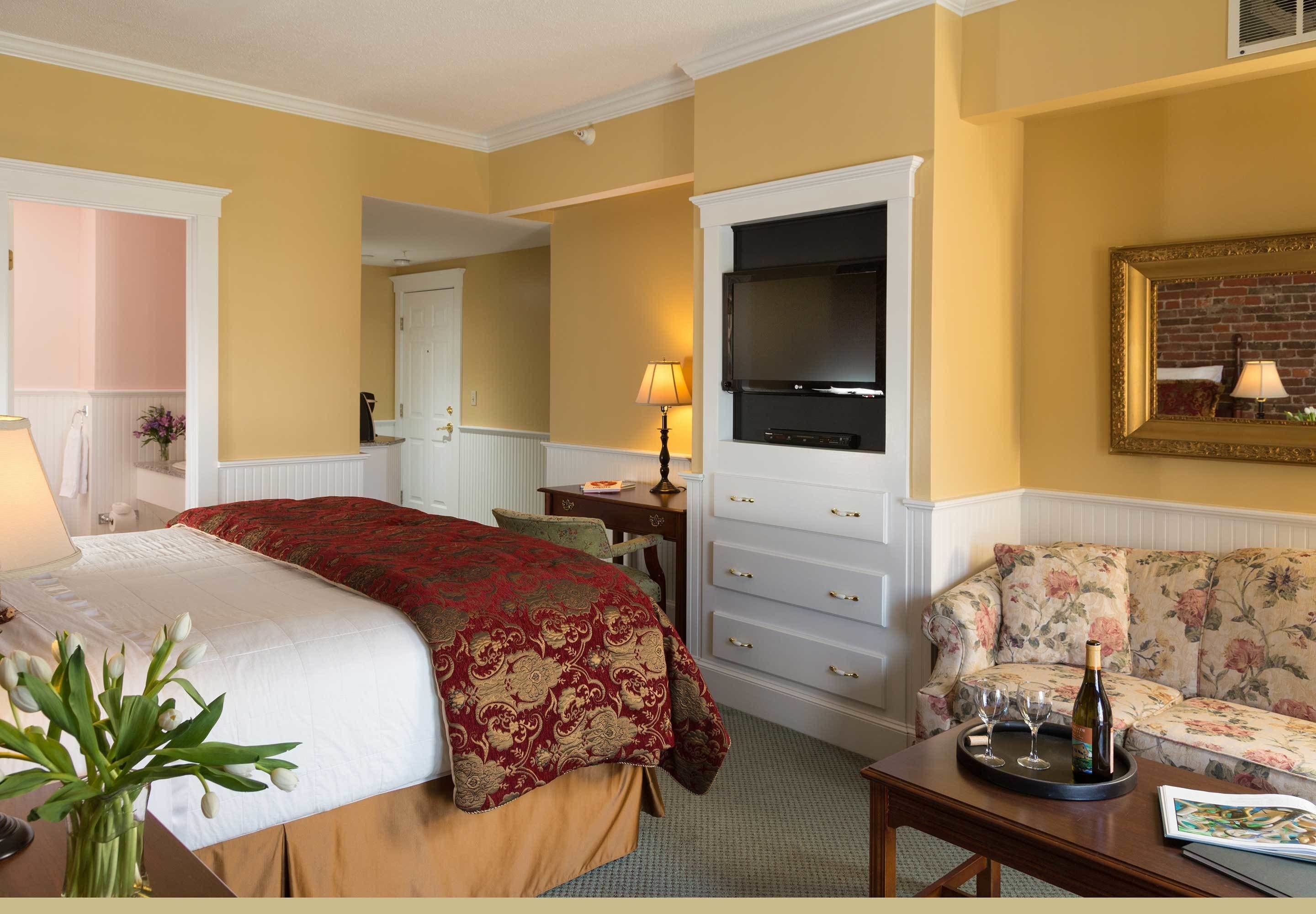 Quarto de hotel com cama, televisão, sofá e secretária com abajur.