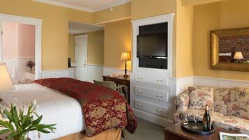 Quarto de hotel com cama, televisão, sofá e secretária com abajur.