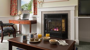 A cozy room with a fireplace, a dining table with breakfast items, a laptop, and a TV. - Lord Camden Inn (Camden)