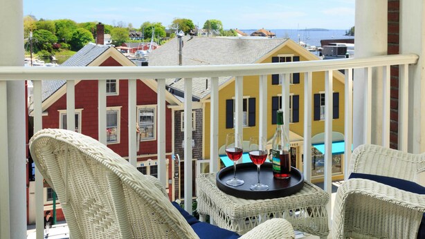 A balcony with wicker furniture, a table with two wine glasses and a bottle, and a view of colorful buildings and a body of water. - Lord Camden Inn (Camden)