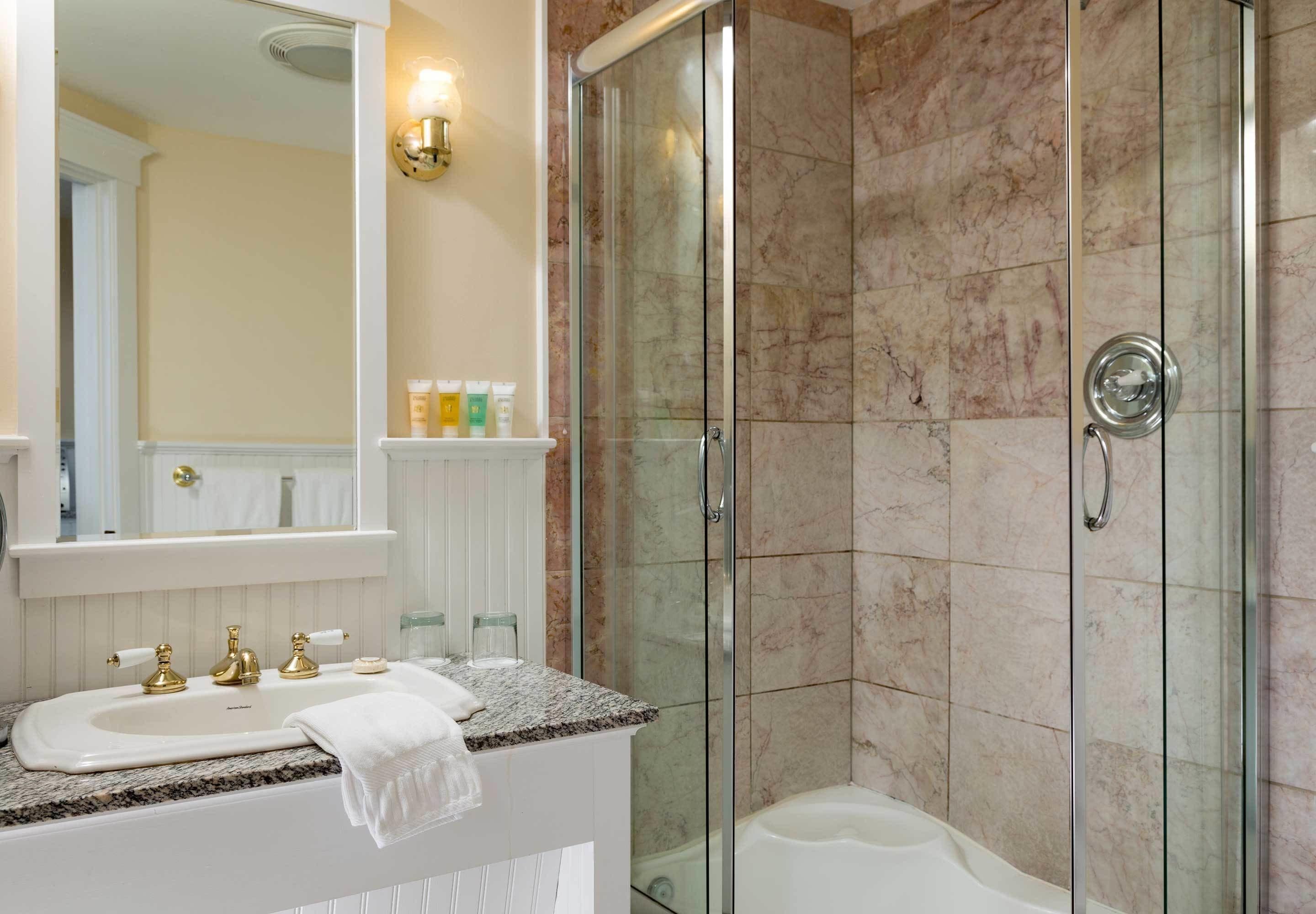 A bathroom with a glass-enclosed shower, a white sink with gold fixtures, and a mirror above the sink.