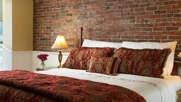 Una cama con una colcha de motivos dorados y rojos, almohadas blancas y un cabecero de madera frente a una pared de ladrillo.