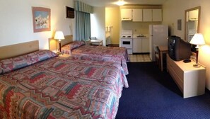 A hotel room with two beds, a small kitchenette, a television, and a desk with a lamp. - Hospitality Inn (Kamloops)