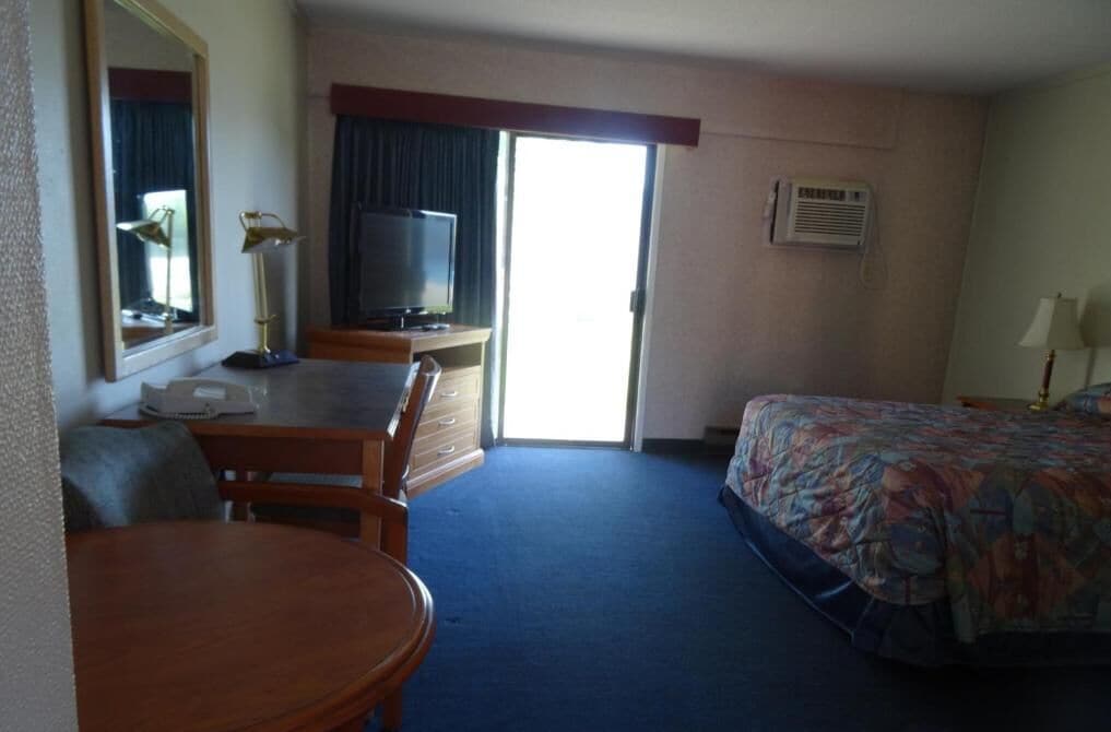 Une chambre d’hôtel comprenant un lit, un bureau avec une chaise, une télévision, un miroir et une fenêtre.