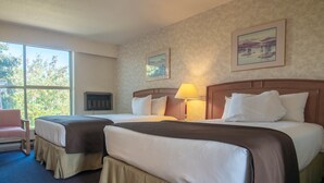 Een hotelkamer met twee bedden, een raam met uitzicht op bomen, een lamp en een schilderij aan de muur.