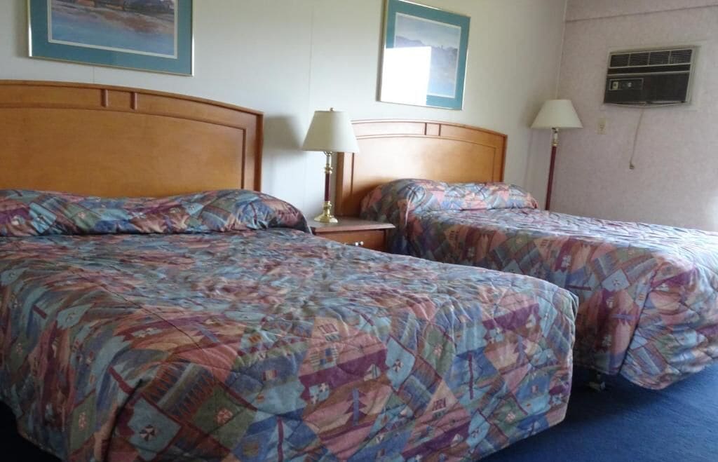Une chambre d’hôtel avec deux lits, chacun agrémenté de draps à motifs, une table de chevet avec une lampe et des œuvres d’art encadrées accrochées aux murs.