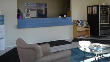 A reception area with a counter, a water dispenser, a refrigerator, a magazine rack, and a glass table with a bowl.