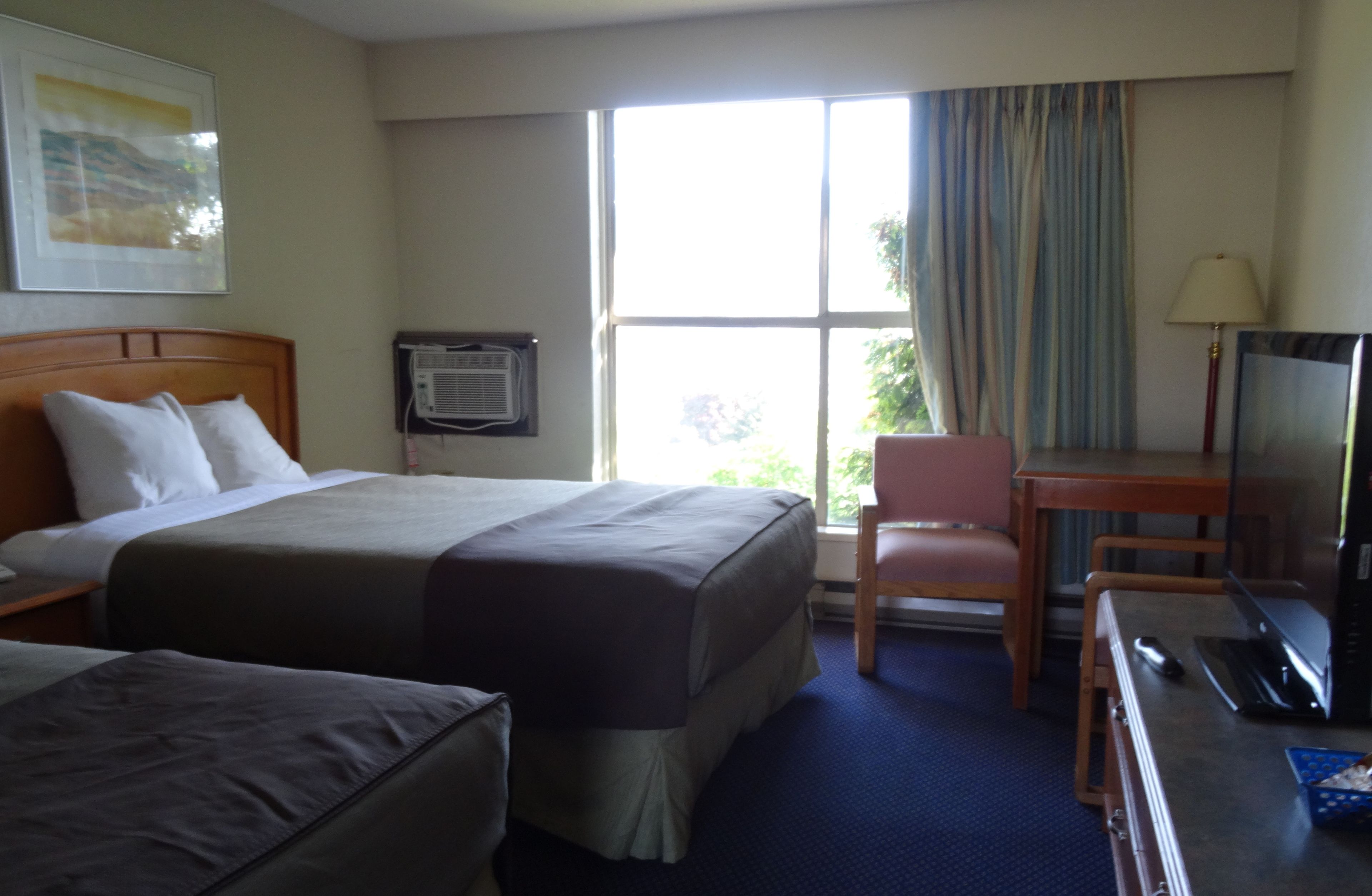 A hotel room with a large bed, a desk with a laptop, a chair, and a television.