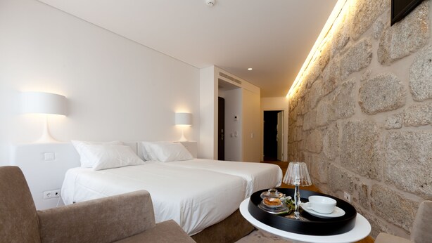A hotel room with two beds, a sofa, a small table with a tray of breakfast items, and a stone wall. - inPatio GuestHouse (Porto)