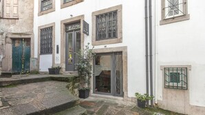A building with a stone facade, multiple windows with metal grilles, and a small garden area with potted plants. - inPatio GuestHouse (Porto)