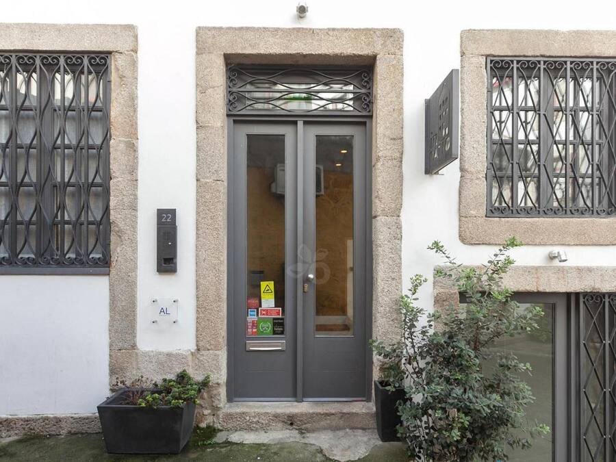 A building with a grey door, two windows with metal bars, and a small planter with plants.