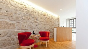 A modern interior with a stone wall, two red chairs, a small round table, and a wooden podium. - inPatio GuestHouse (Porto)