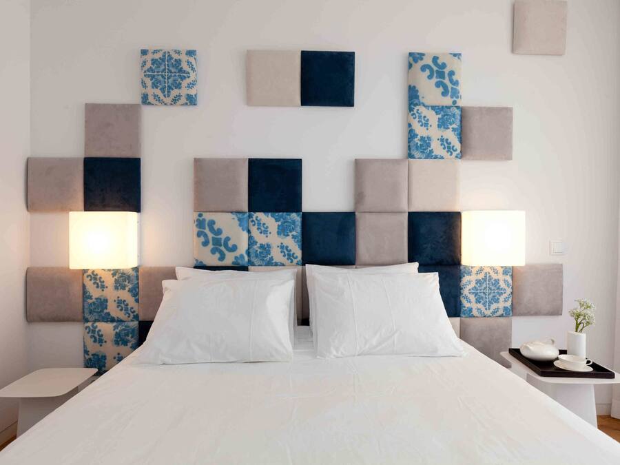 A modern hotel room with a large bed, two bedside tables, and a headboard with patterned tiles.