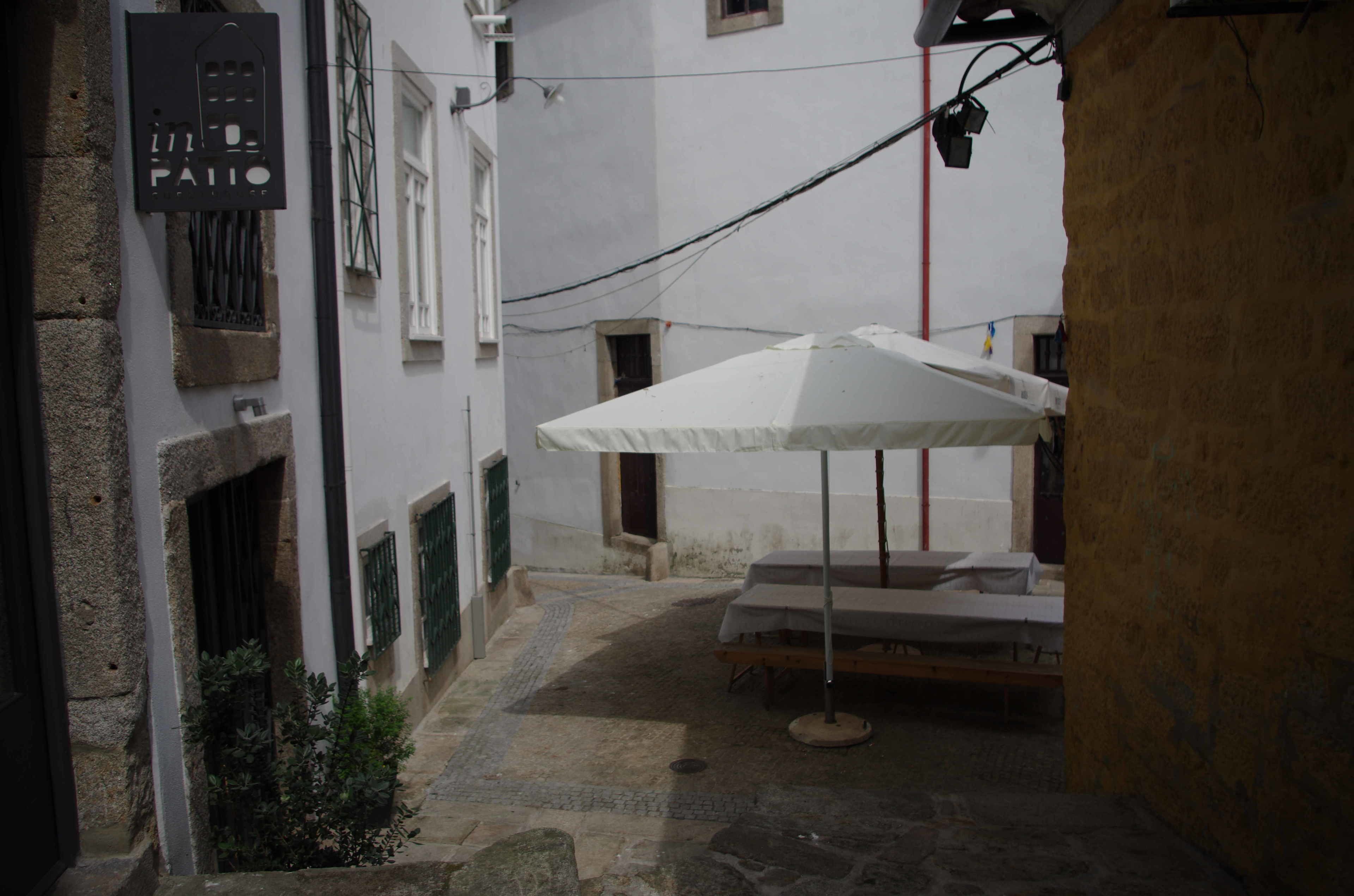 Un patio estrecho con una sombrilla blanca y una cama.