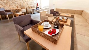 A modern lounge area with a stone wall, comfortable seating, and a tray with breakfast items. - inPatio GuestHouse (Porto)