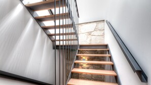 A modern staircase with wooden steps and metal railings, leading to a stone wall. - inPatio GuestHouse (Porto)