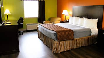 A hotel room with a bed, two chairs, a desk with a computer, and a window with curtains.