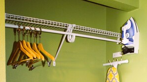 A room with a green wall, a wooden floor, a clothes rack with hangers, and an ironing board with an iron. - Scottish Inns Killeen near Fort Cavazos (Killeen)