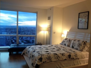 A bedroom with a large window, a bed with floral bedding, a bedside table, and a nightstand.
