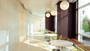 A modern interior with a long corridor, white tables, and chairs, and large windows allowing natural light. - Green Suites (Jersey City)