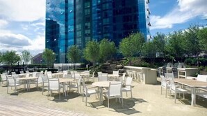 An outdoor patio area with tables and chairs, a stone wall, and a modern glass building in the background. - Green Suites (Jersey City)