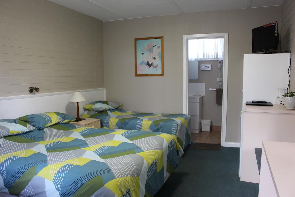 A hotel room with two beds, a desk, a lamp, a television, and a bathroom visible through an open door.
