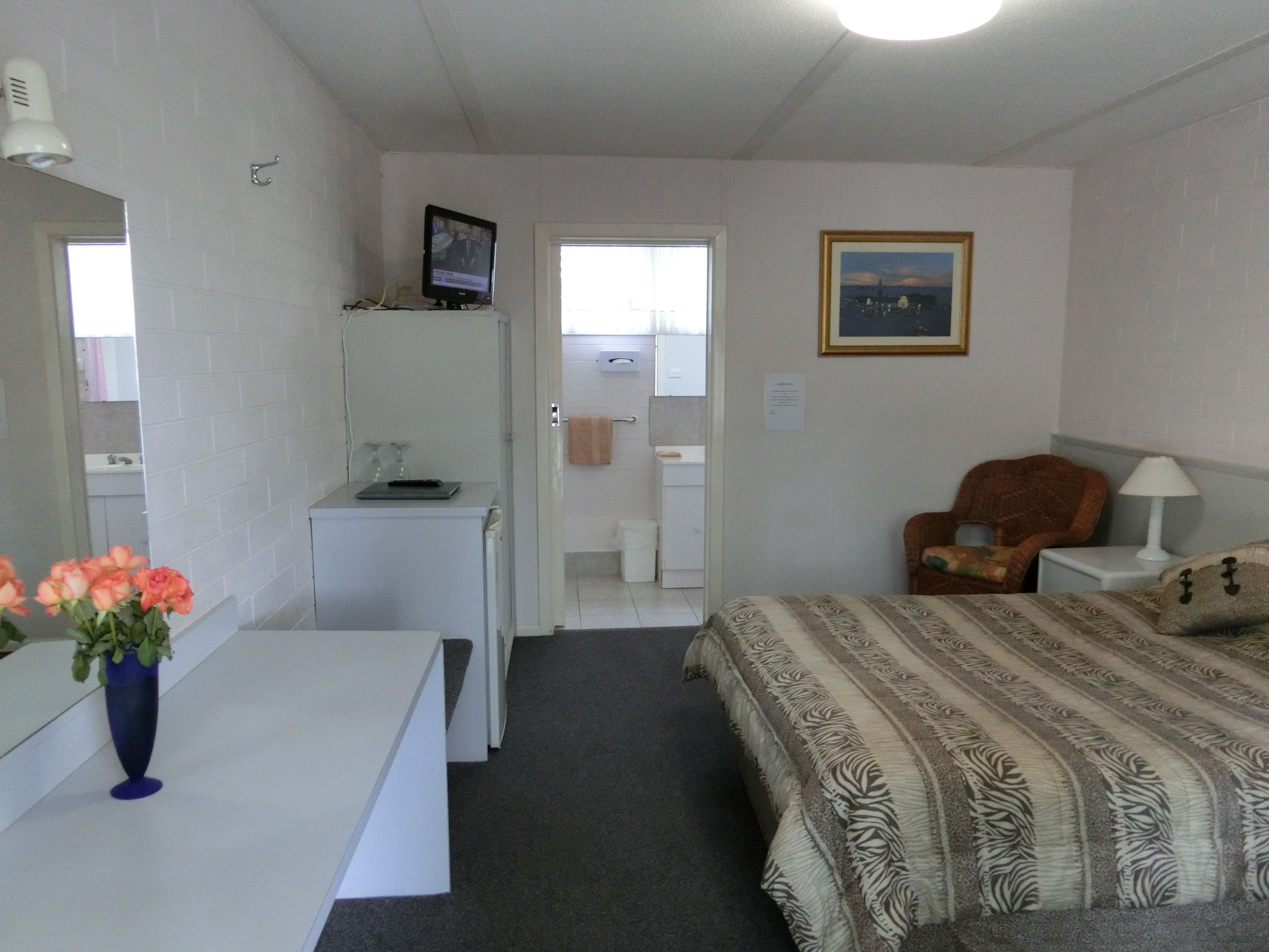 Ein Hotelzimmer mit Bett, Schreibtisch, Stuhl, Fernseher und einem durchgegangenen Tür sichtbaren Badezimmer.