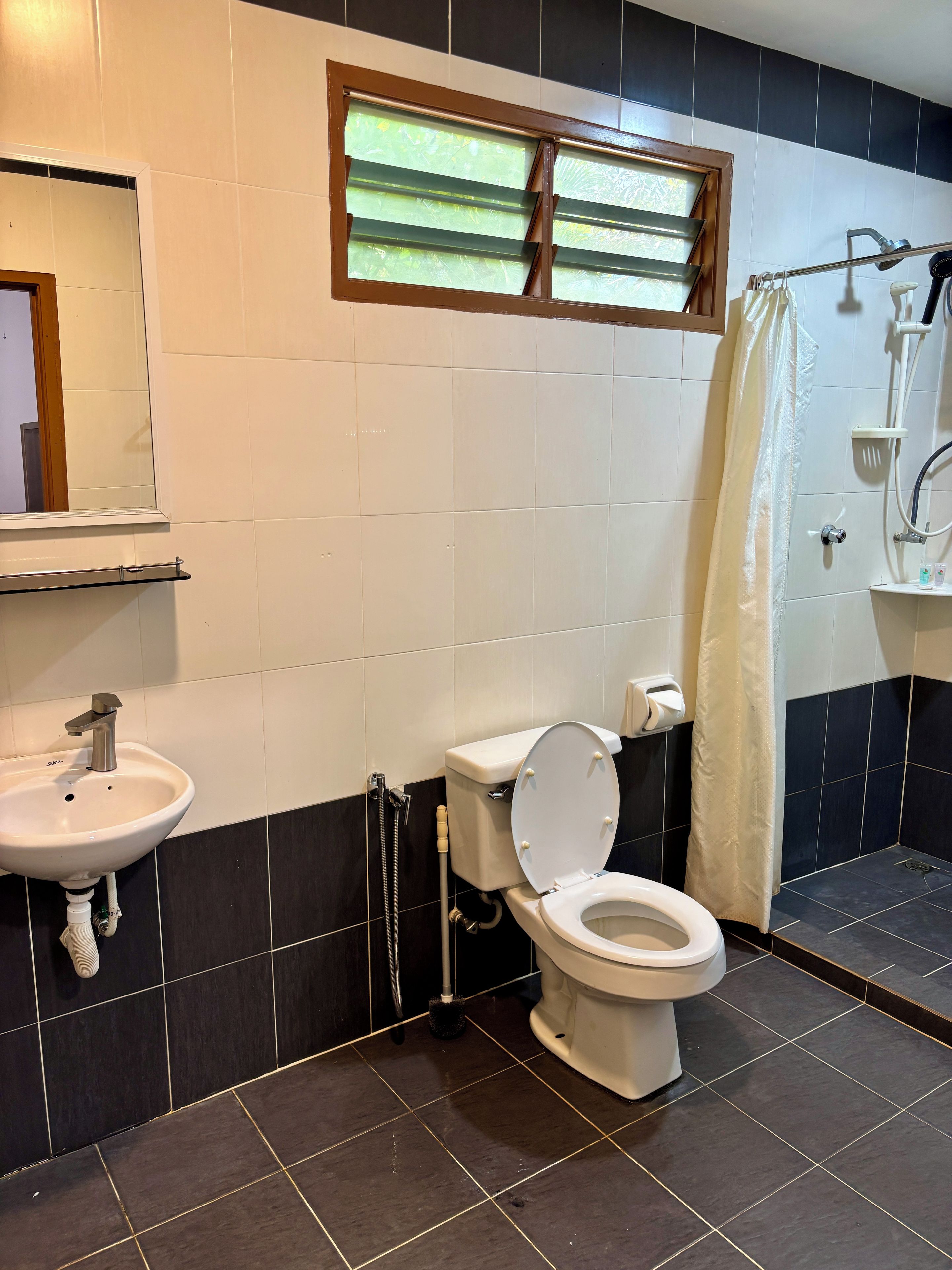 Un baño con inodoro, lavabo, ducha y ventana con persianas.