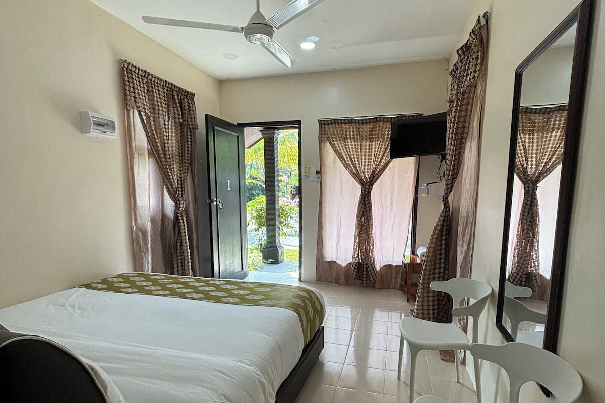 A hotel room with a bed, a ceiling fan, a television, and a seating area with chairs.